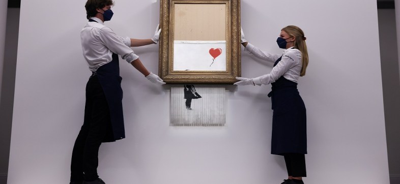 FILE PHOTO: A gallery assistant poses by 'Love is in the Bin', an artwork by Banksy, which will be for sale in an auction, at Sotheby's in London, Britain, September 3, 2021.