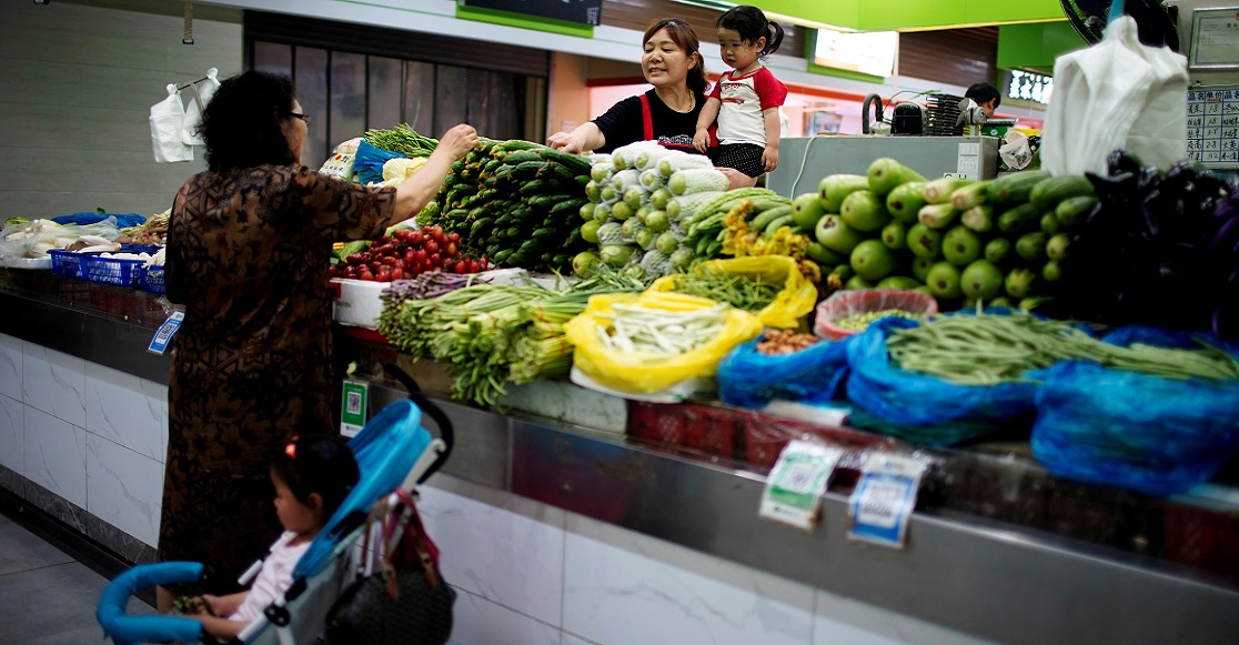 FILE PHOTO: Two grandmothers with their granddaughter trade vegetables at a market on the outskirts of Shanghai, China June 3, 2021. 